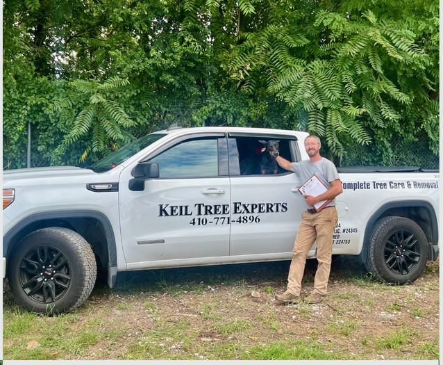 A man is standing in front of a truck that says keil tree experts.