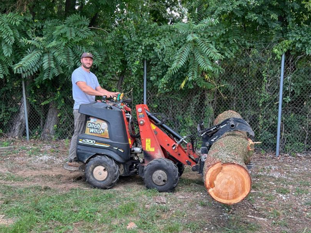 A man is driving a tractor next to a large log.