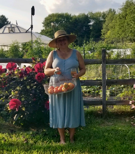 A woman in a blue dress is holding a basket of fruit and a glass of wine.