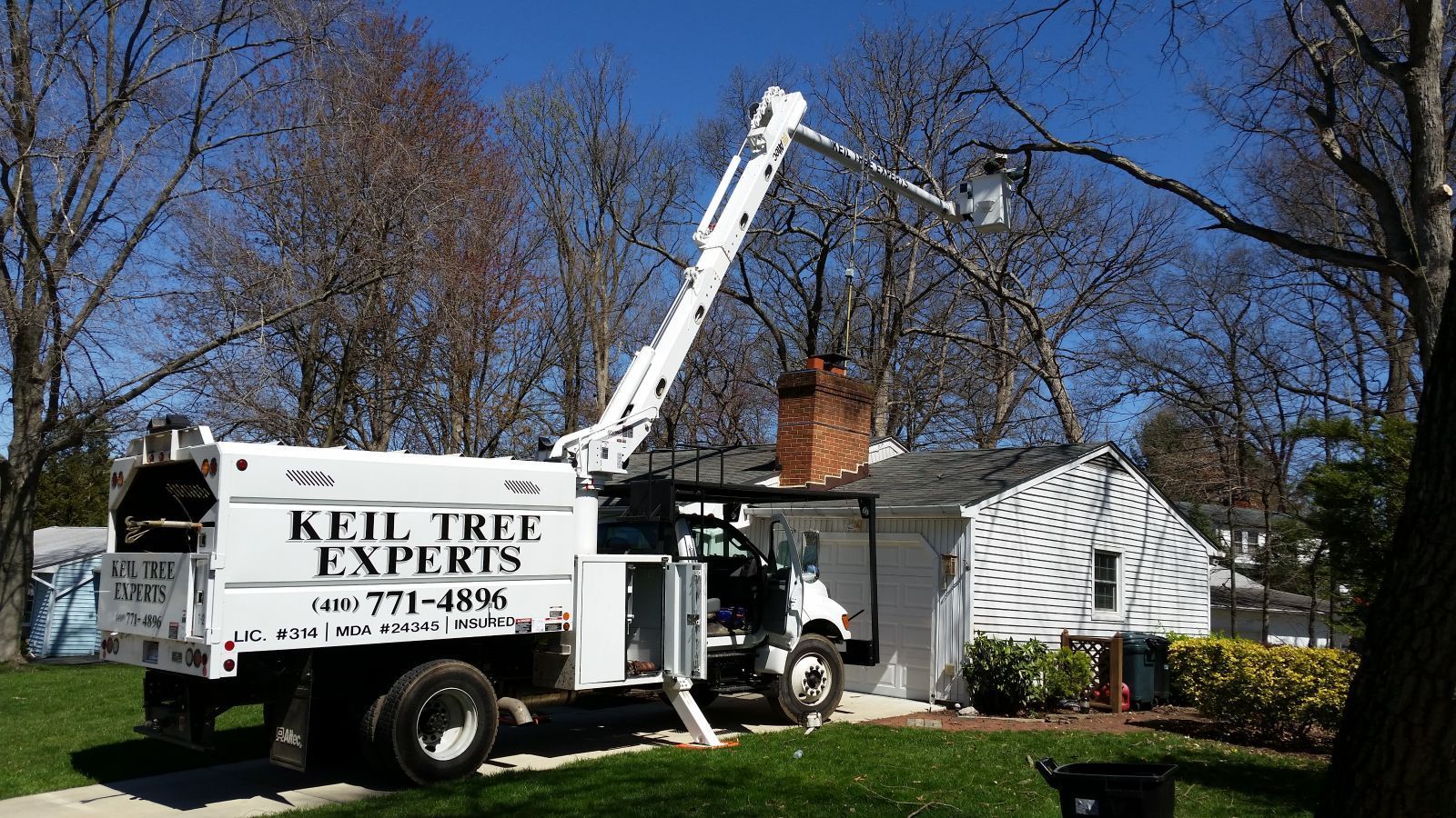 A white truck with a crane attached to it is parked in front of a house.