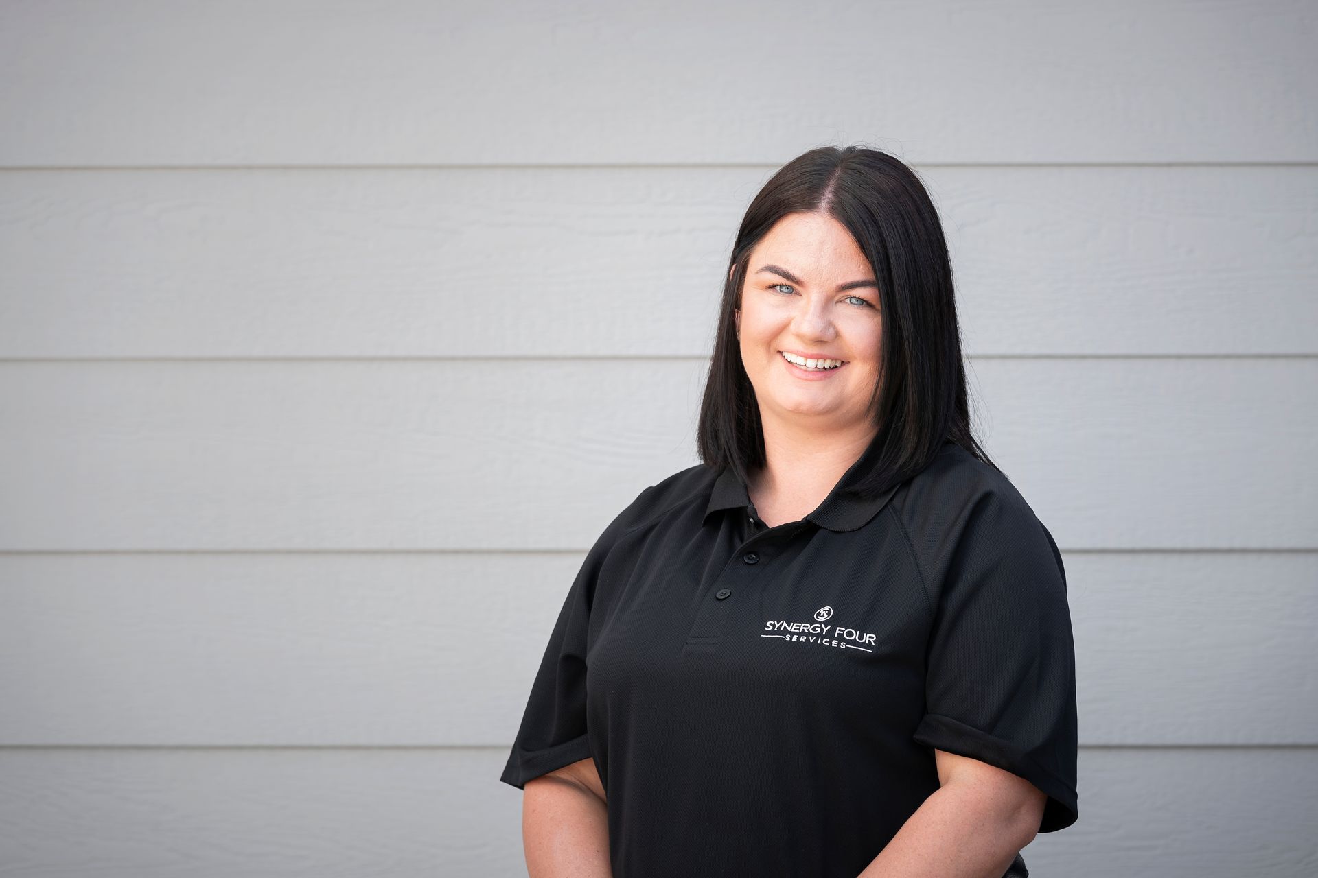 A woman in a black shirt is standing in front of a gray wall.