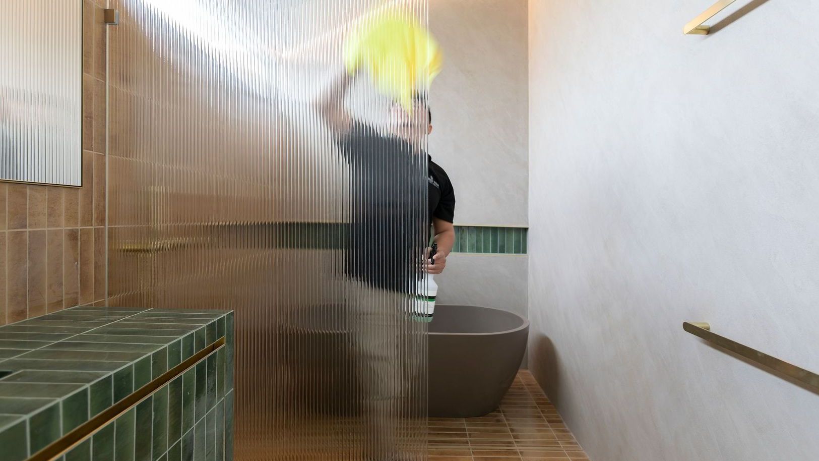 A man is standing in a bathroom behind a clear shower curtain.