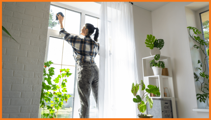 A woman is cleaning a window in a living room.