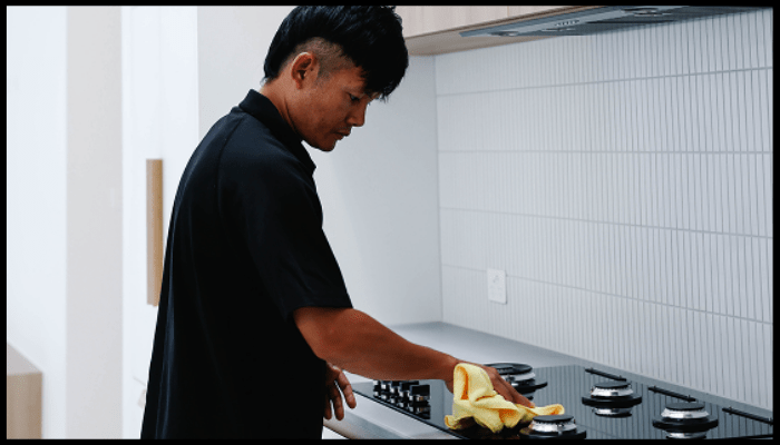 A man is cleaning a stove top with a cloth in a kitchen.