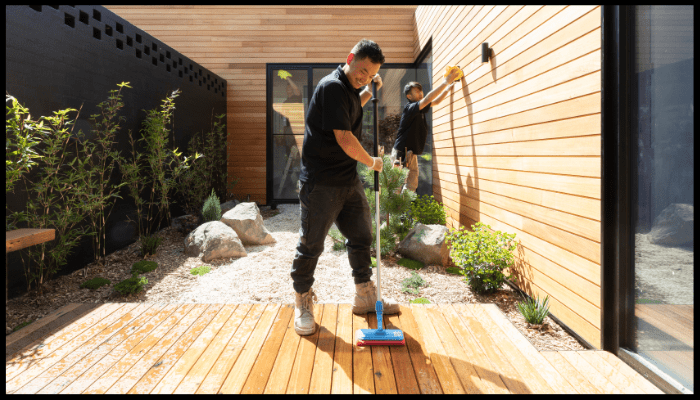 A man is cleaning a wooden deck with a broom.