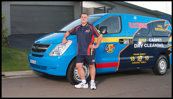 A man standing in front of a blue van that says dry cleaning