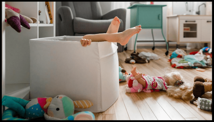 Child playing in a toy storage bin in a cluttered room, showing the need for regular deep cleaning in homes with kids.