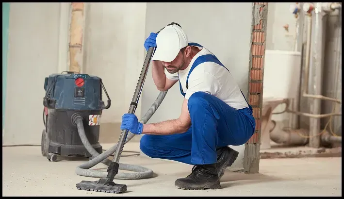 Worker vacuuming construction dust in an unfinished building.