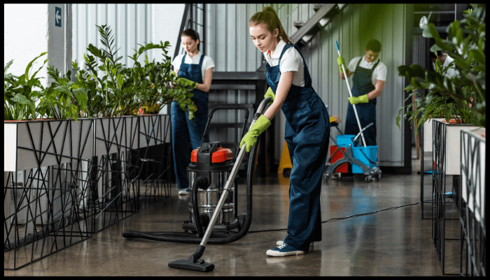 Professional strata cleaning team vacuuming and mopping common indoor areas with plants and stairs, using commercial-grade equipment.