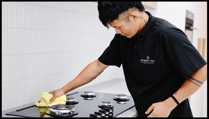 Synergy Four Services cleaner performing a detailed kitchen stovetop clean during a residential deep cleaning session.