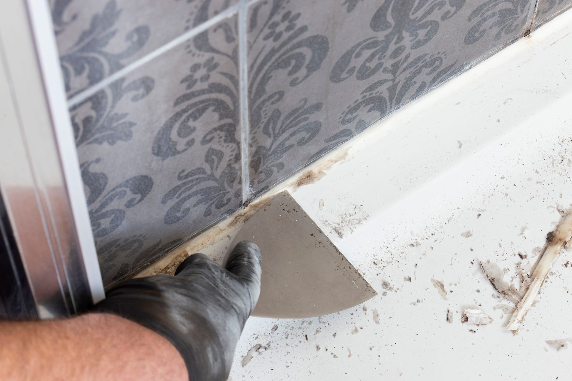 A person is cleaning a bathroom wall with a spatula.