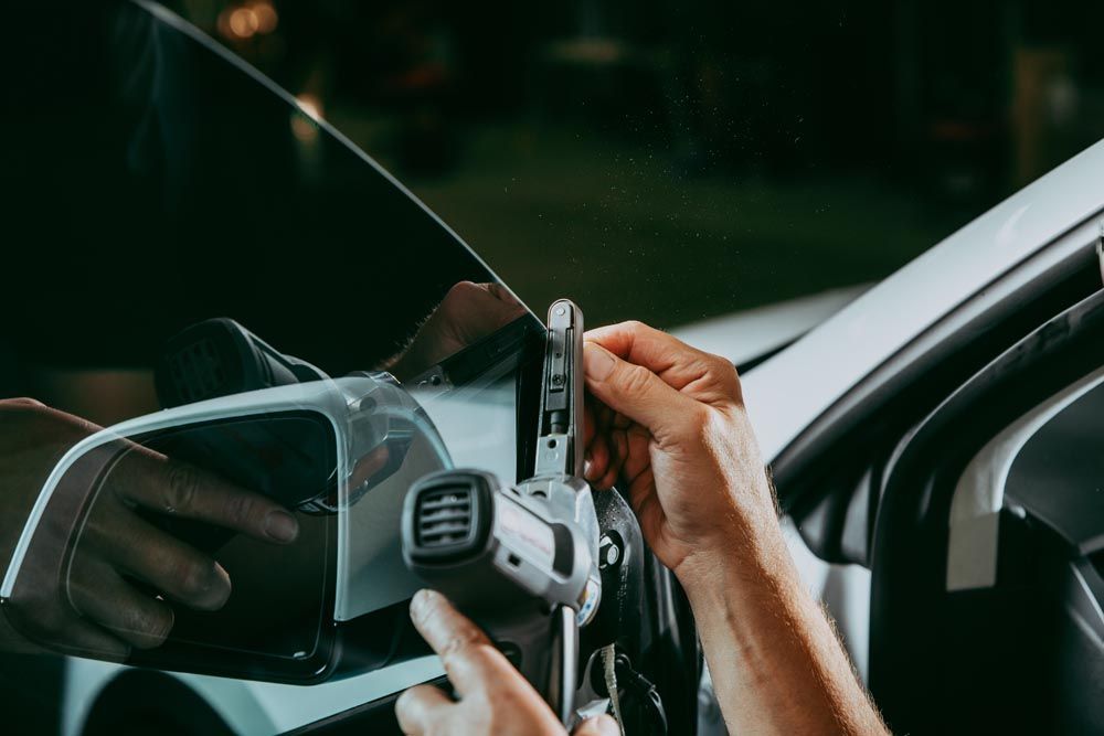 Person using a tool to work on a car's window, likely installing window tint. White car, nighttime setting.