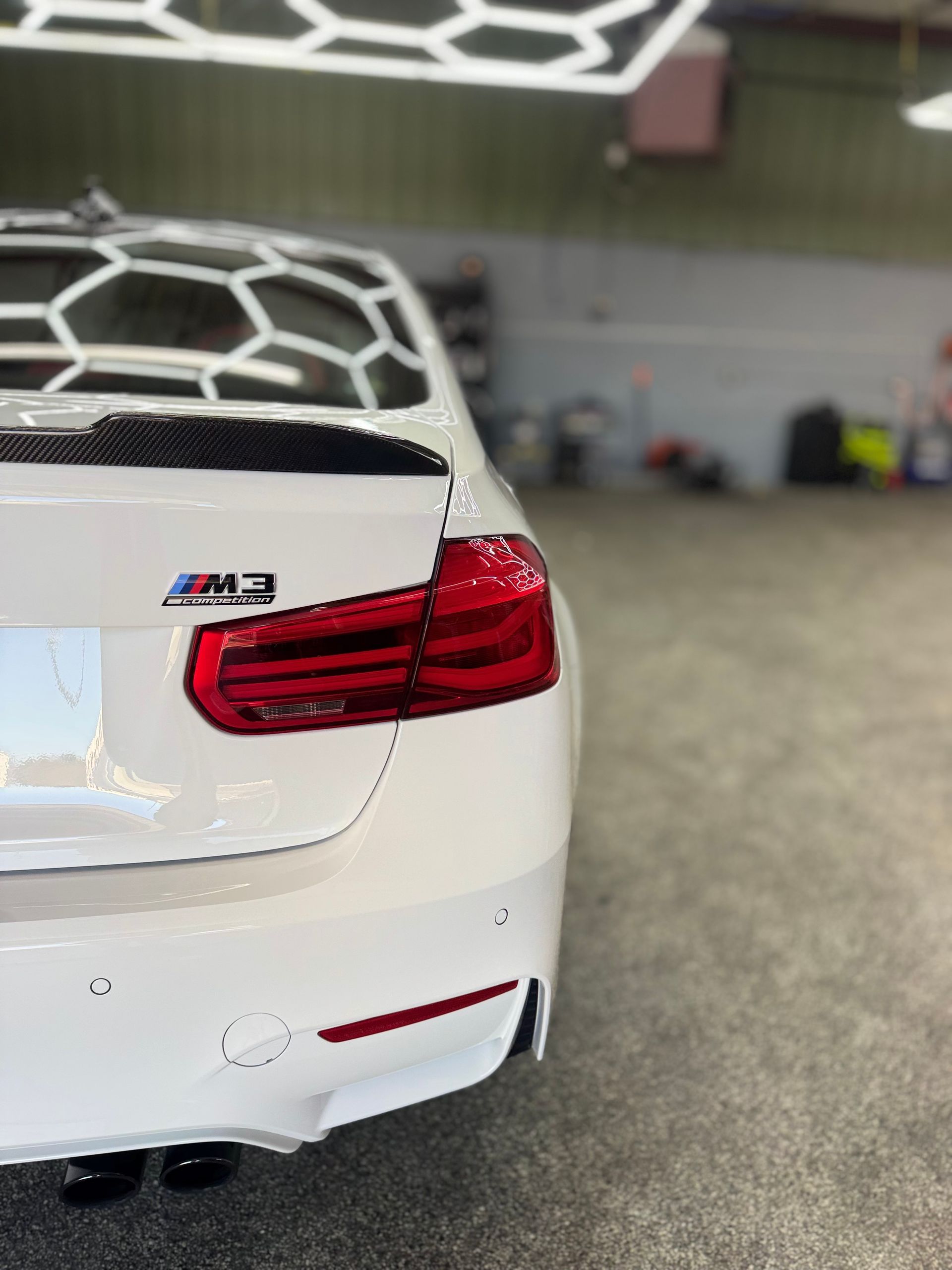 White BMW  rear view in a well-lit shop, showing taillights and M2 badge.