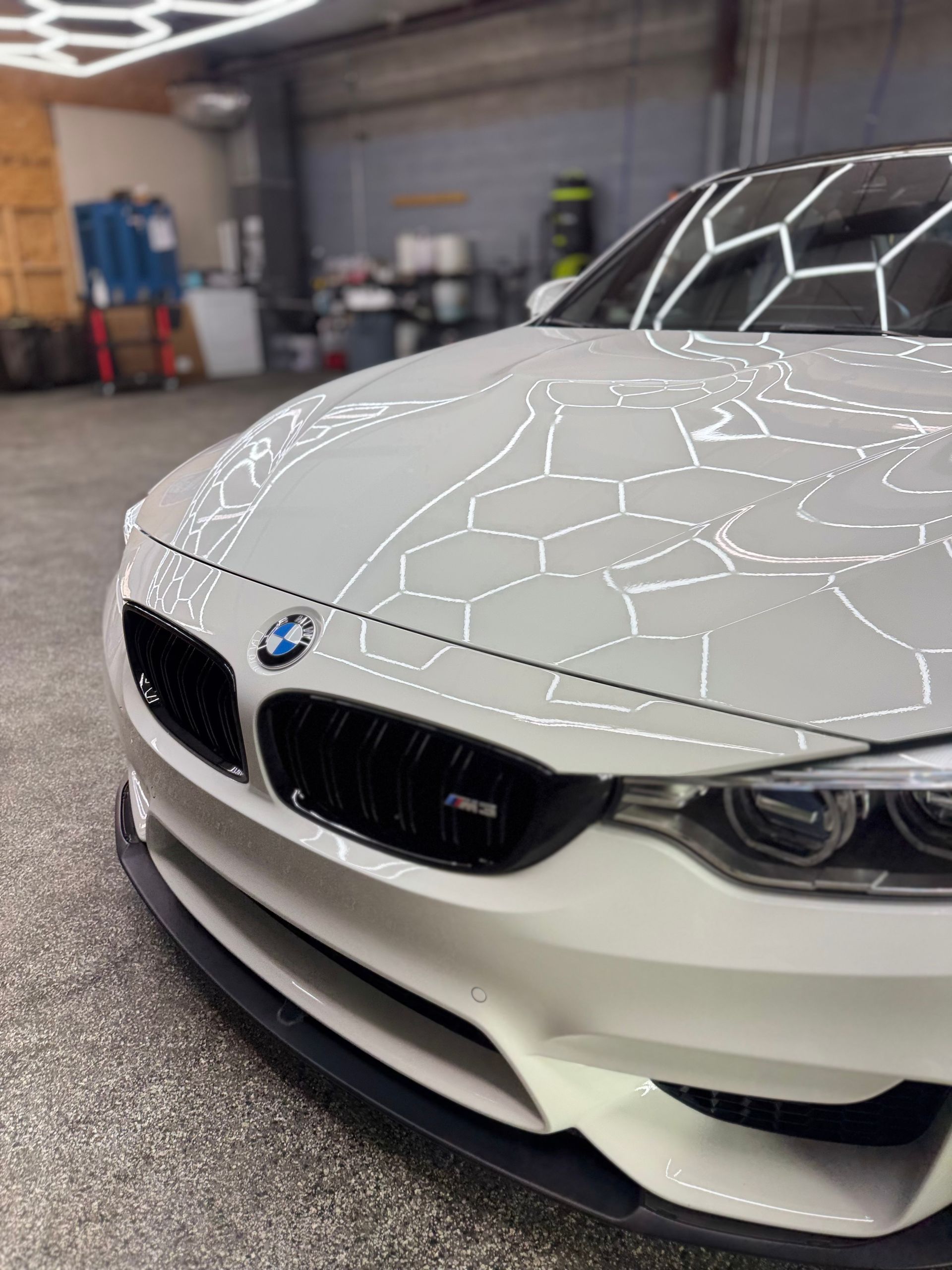 White BMW sports car in a garage with black front grill, illuminated by overhead lights.