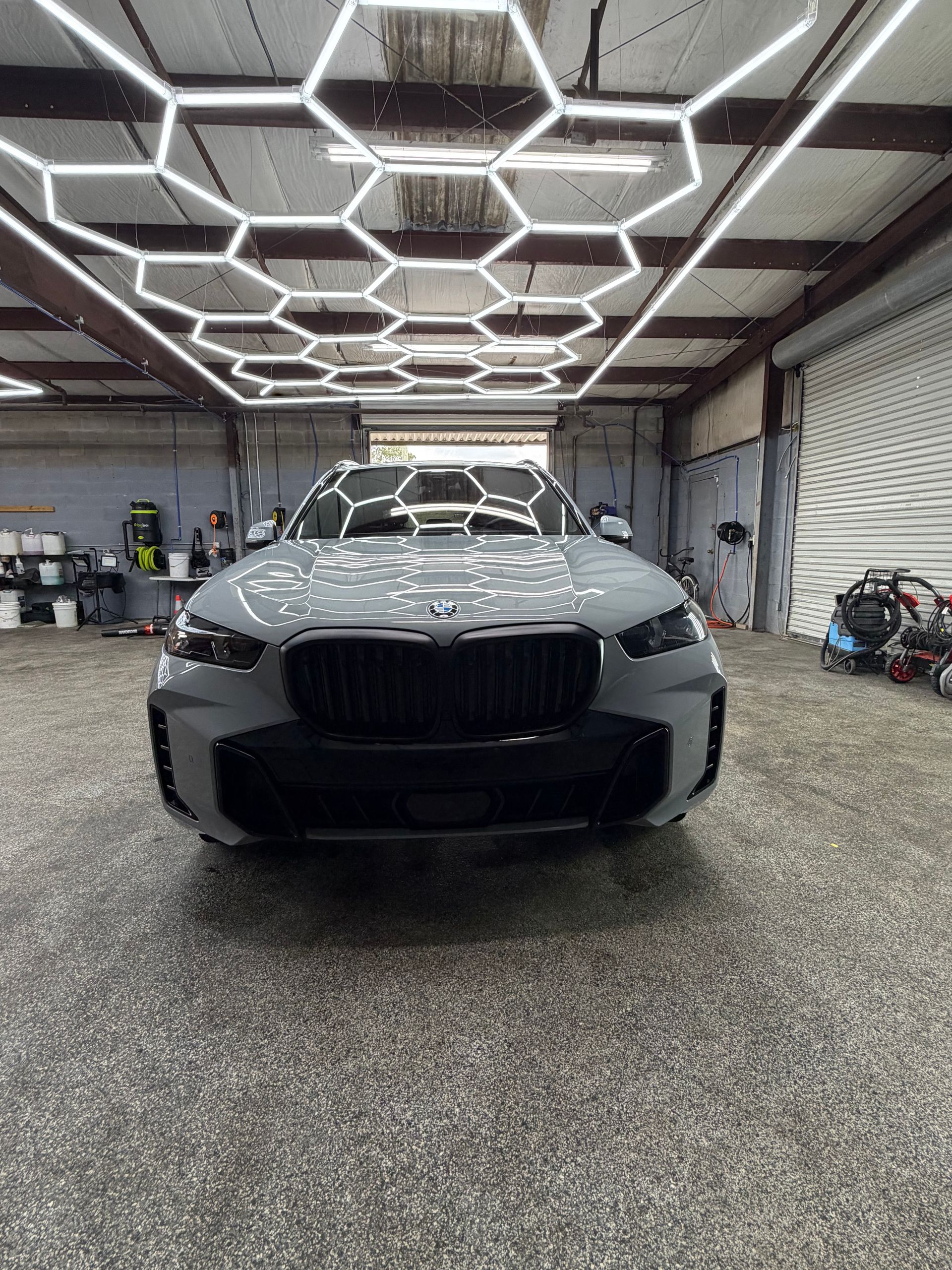 A gray BMW SUV parked inside a garage, with hexagon-shaped lights on the ceiling.