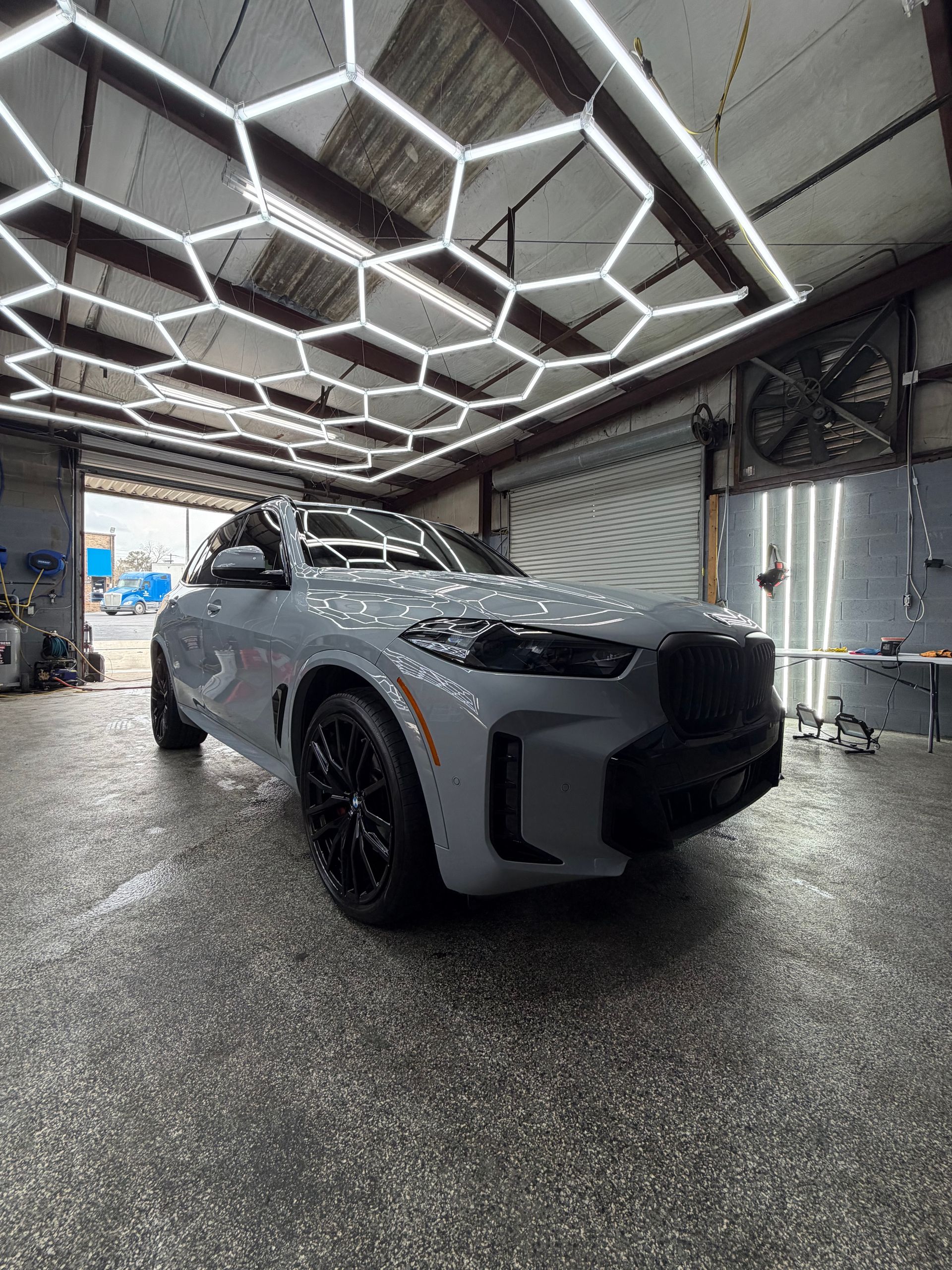 Gray BMW SUV in a garage with hexagonal lights, black wheels, and a gray floor.