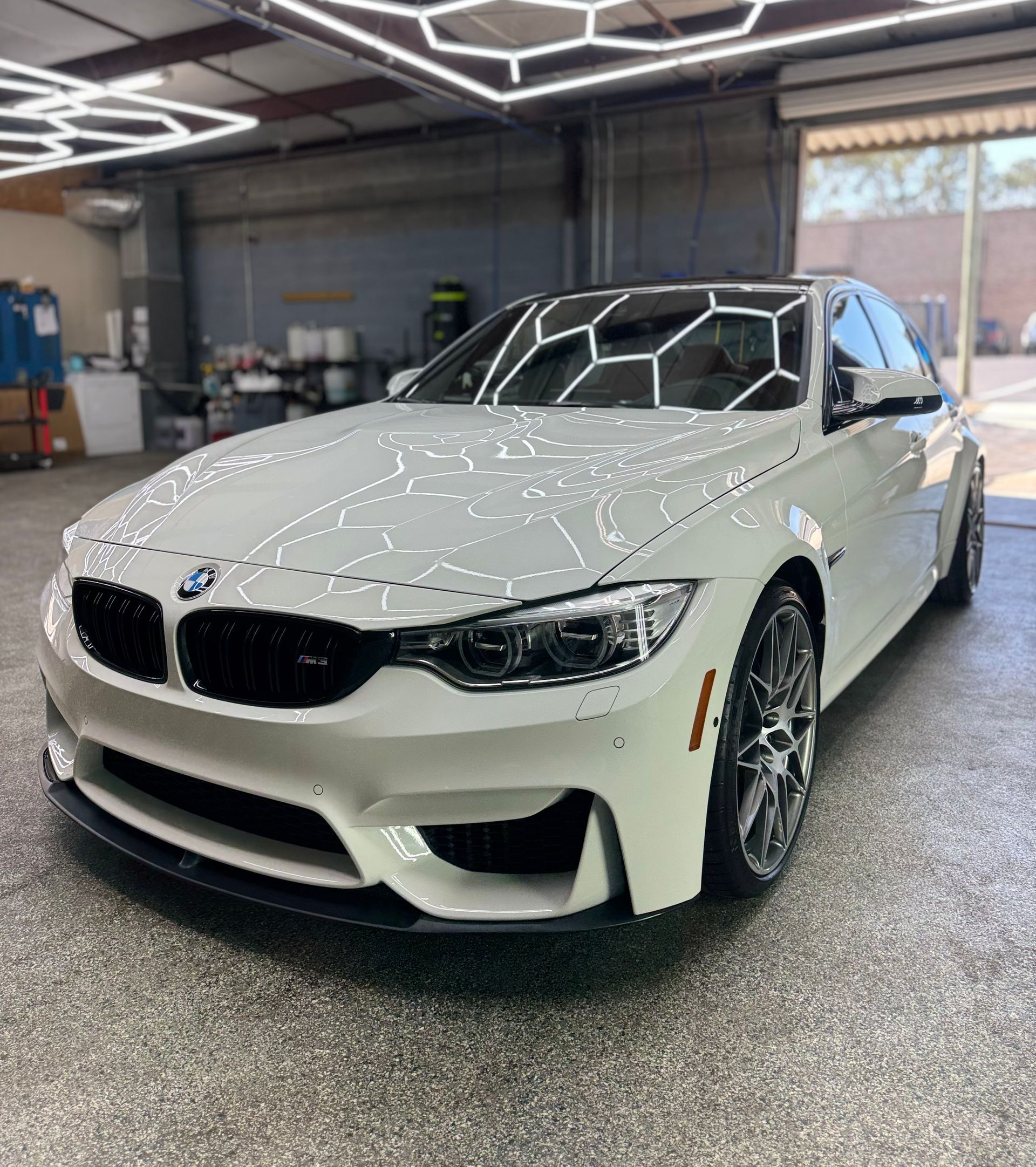 White BMW car under hexagon lights in a car detailing bay.