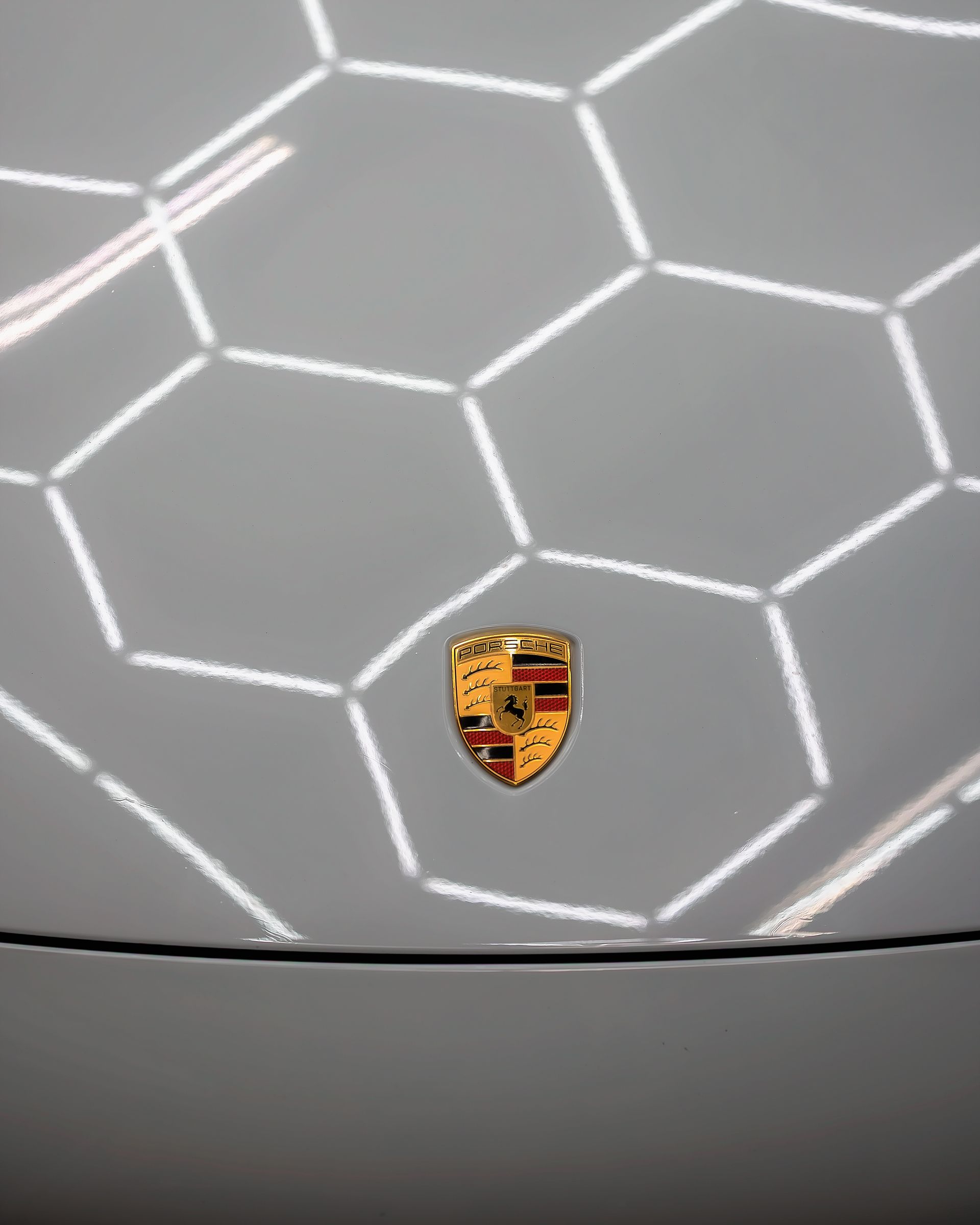 Porsche emblem on a white car hood, with a honeycomb light reflection.