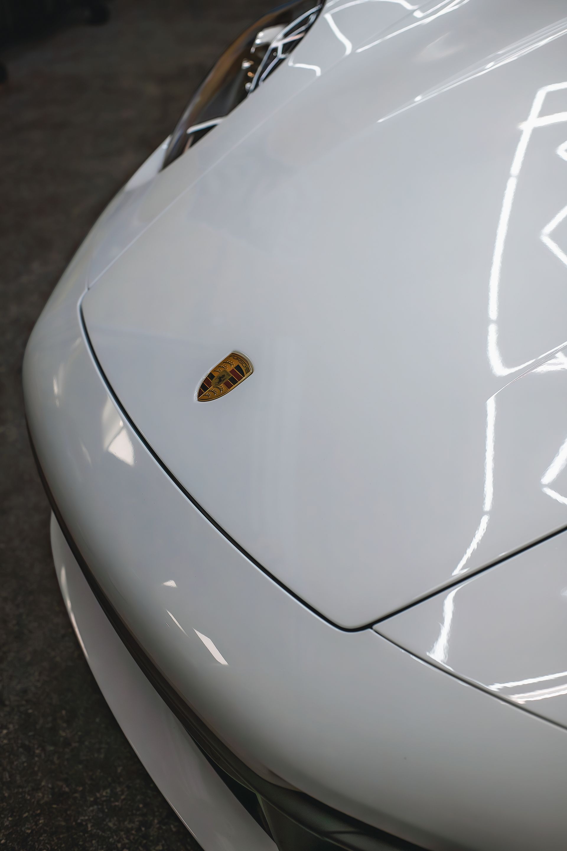 White Porsche hood with the emblem at the center, reflecting overhead lights.