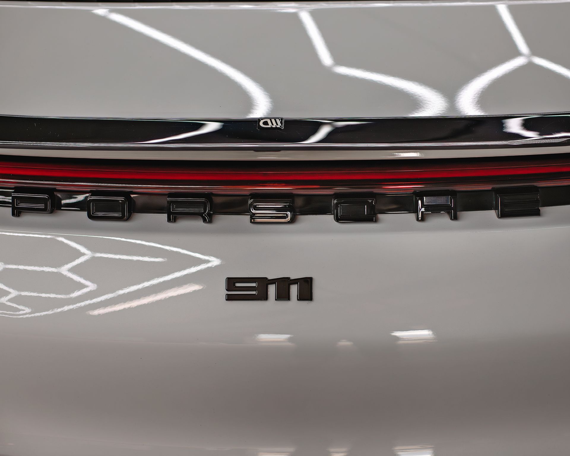 Close-up of the rear of a white Porsche 911 car, with the model name in black lettering.