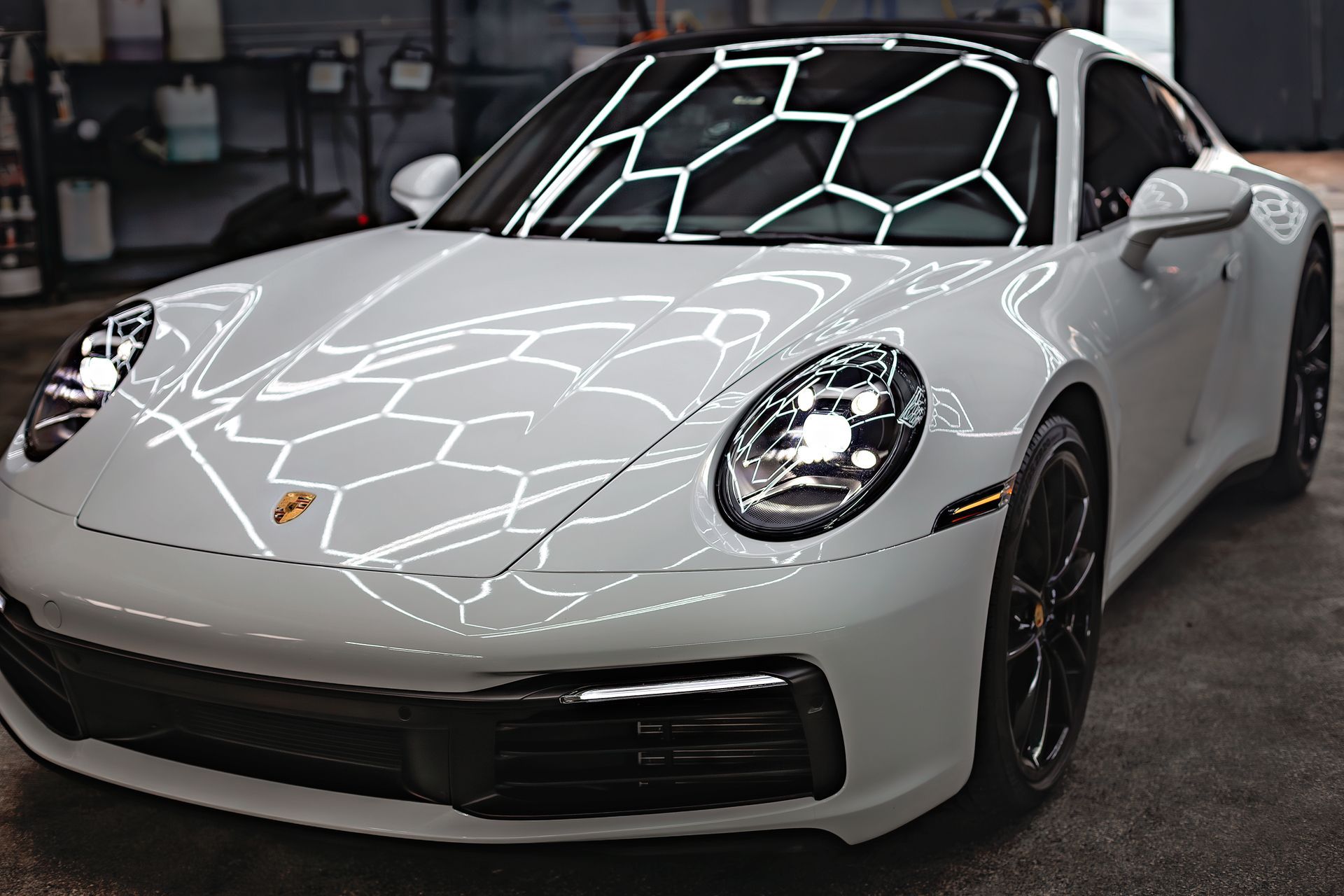 White Porsche sports car in a garage with shiny finish, reflecting overhead lighting.