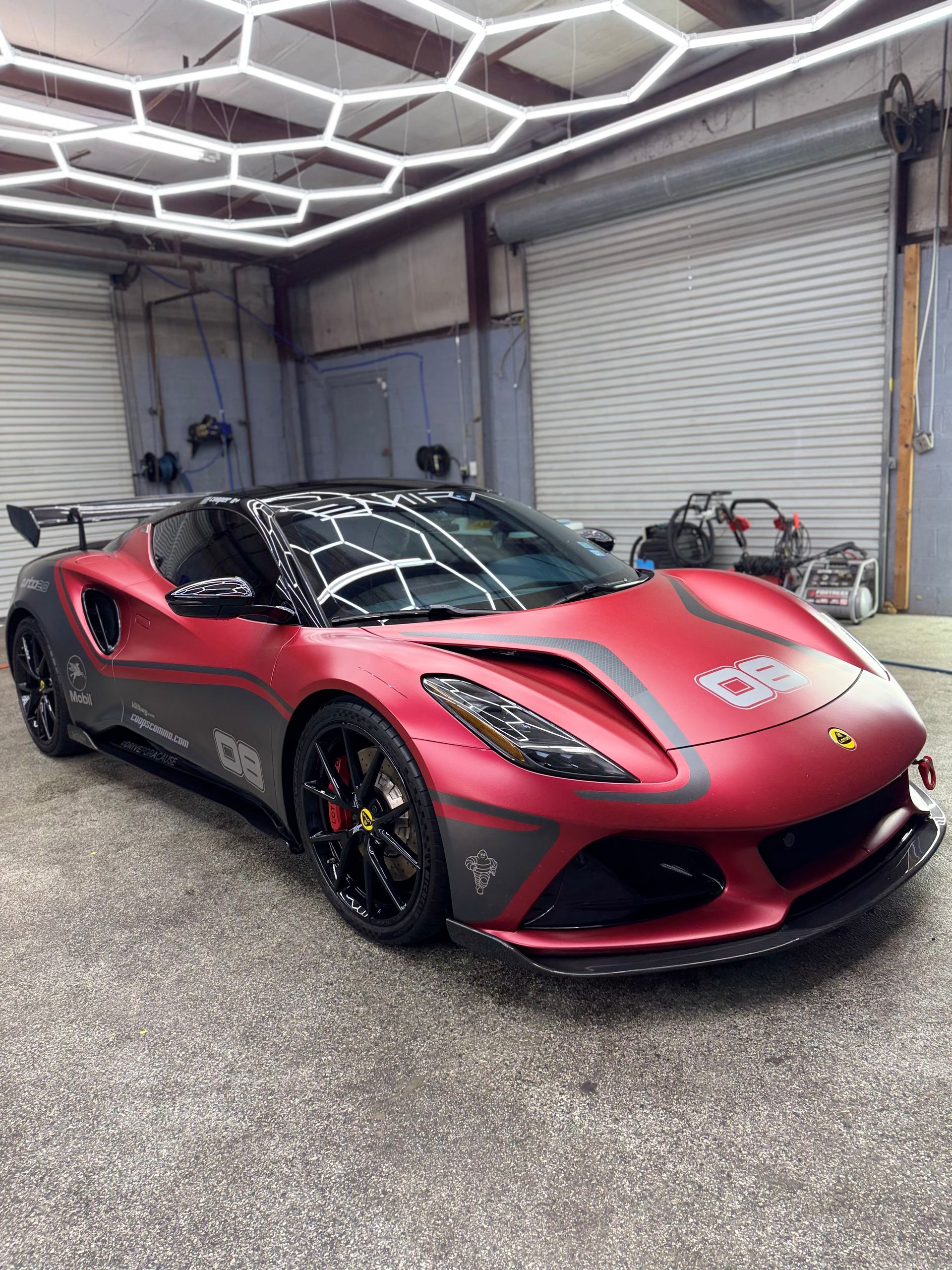 Red and gray sports car in a garage with a black roof and black wheels, under hexagonal lights.