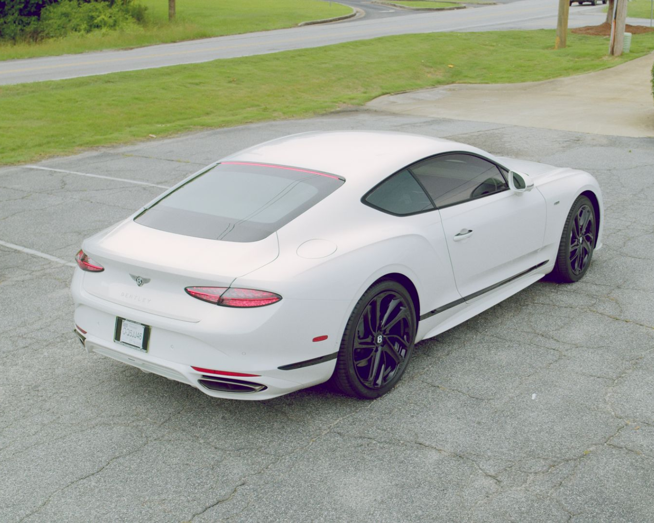 White Bentley coupe parked on a paved lot with a grassy area in the background.