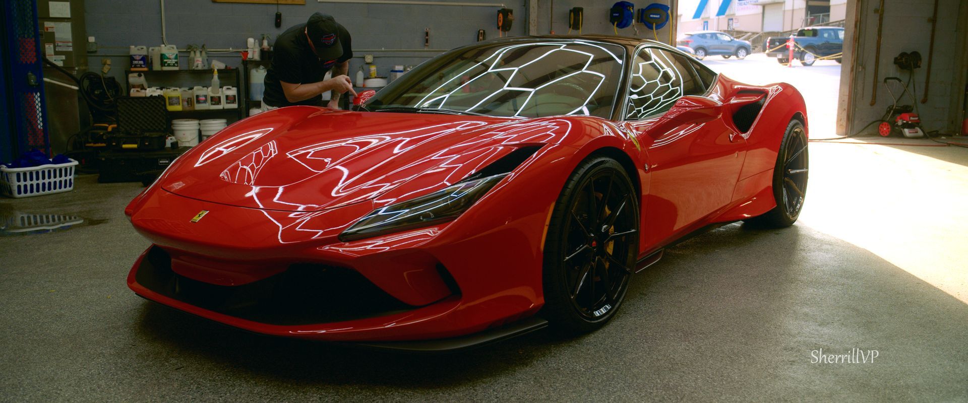 A red Ferrari sportscar being detailed inside a garage. A person is working on the car.