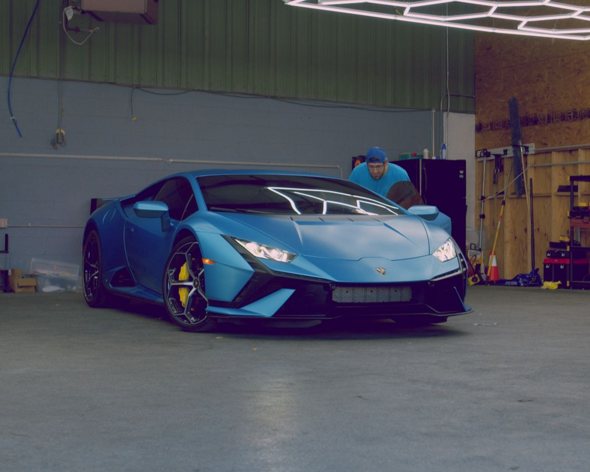 Blue Lamborghini in a garage, a person leaning into it.