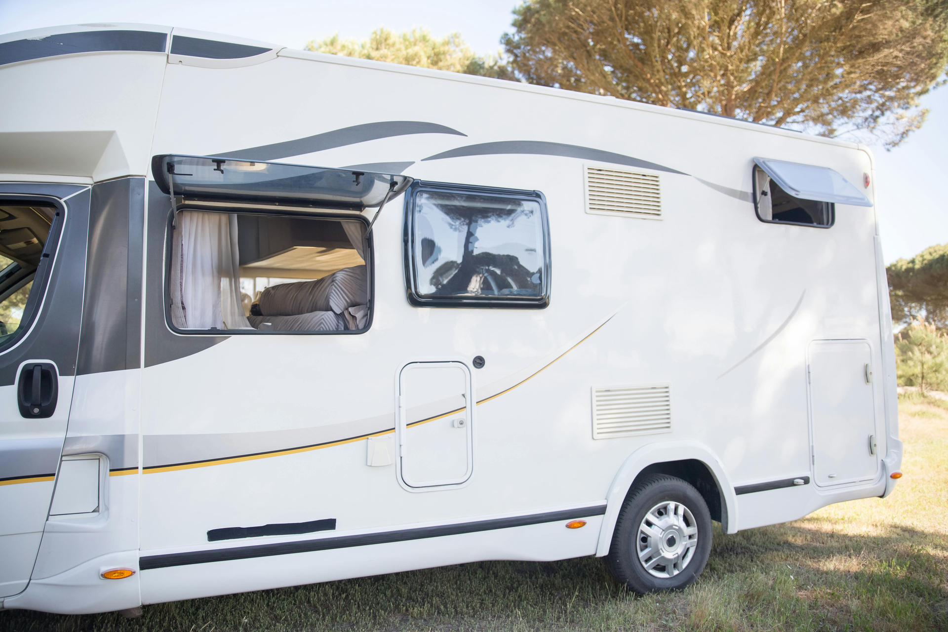 White RV parked on grass, with open windows and awnings, under a blue sky.