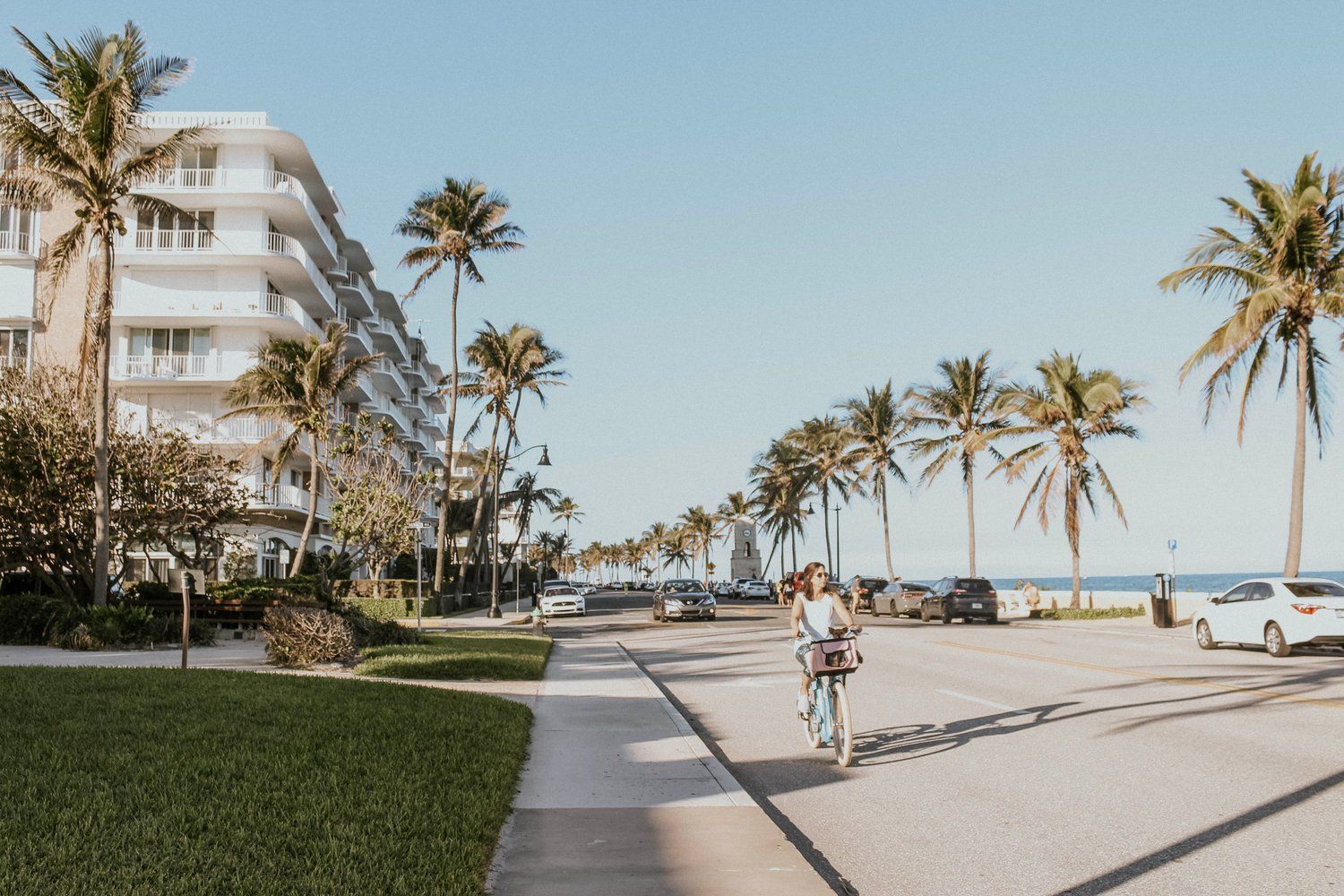 Una mujer anda en bicicleta por una acera junto a palmeras.