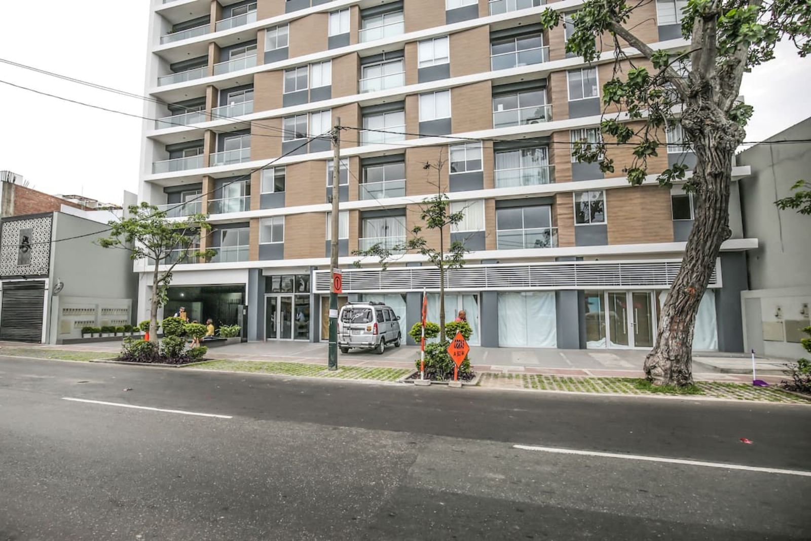 Un automóvil está estacionado frente a un edificio alto al costado de la carretera.