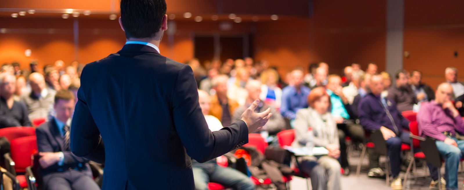 Un hombre está dando una presentación ante un gran grupo de personas en una sala de conferencias.