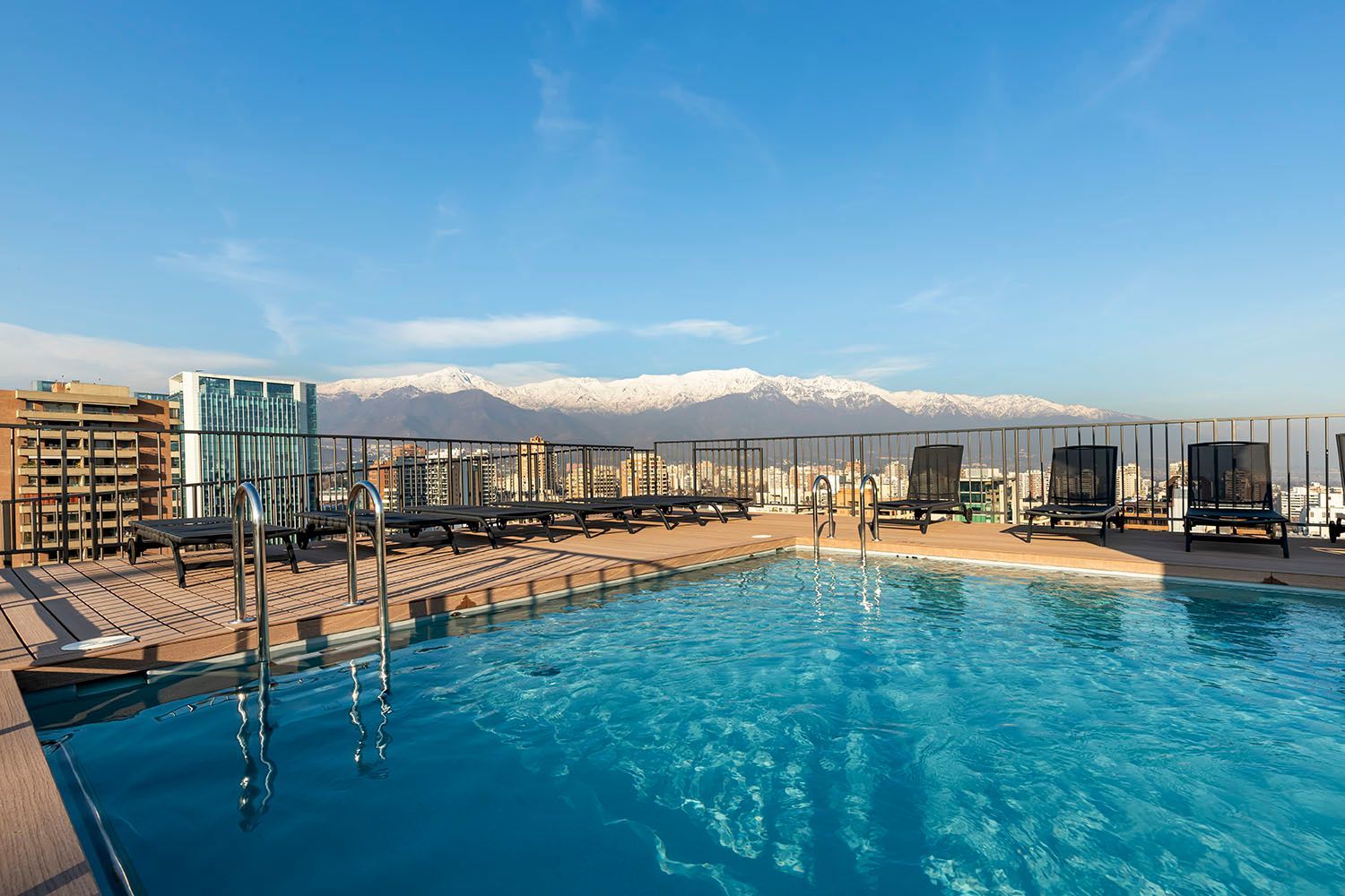 Nueva las Condes. Una gran piscina en lo alto de un edificio con las montañas al fondo.