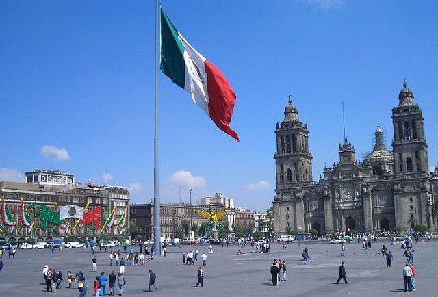 Una bandera mexicana ondea frente a un gran edificio.