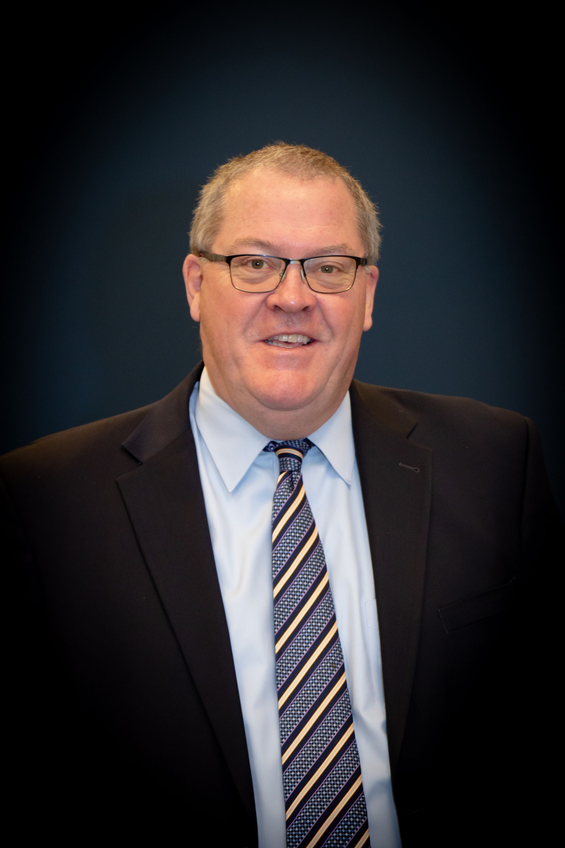 Man in a suit and tie, smiling, indoors.