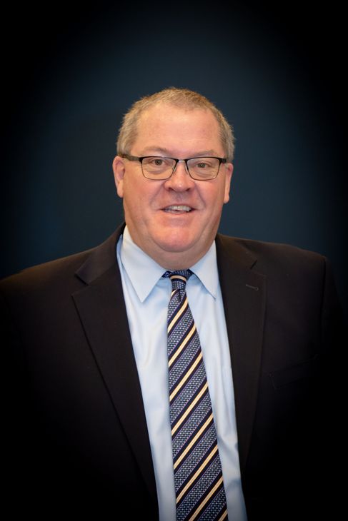 Man in a suit and tie, smiling, indoors.