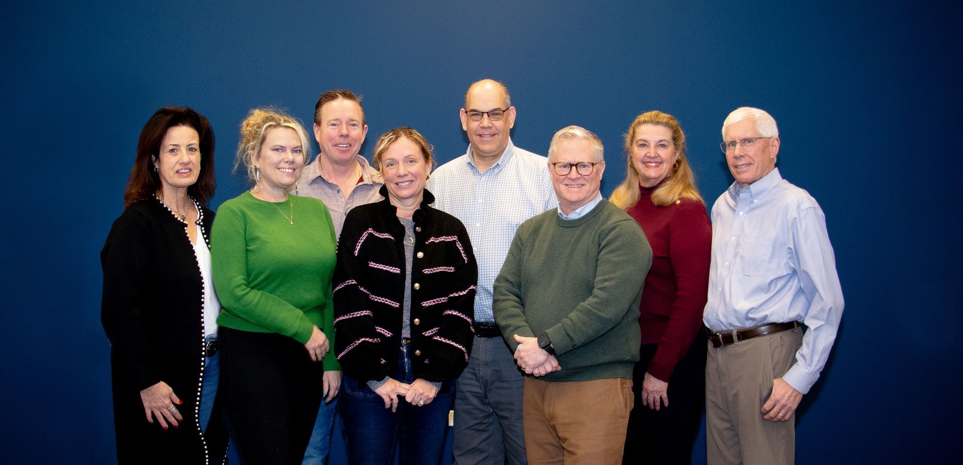 Group of nine people posing in front of a blue background.