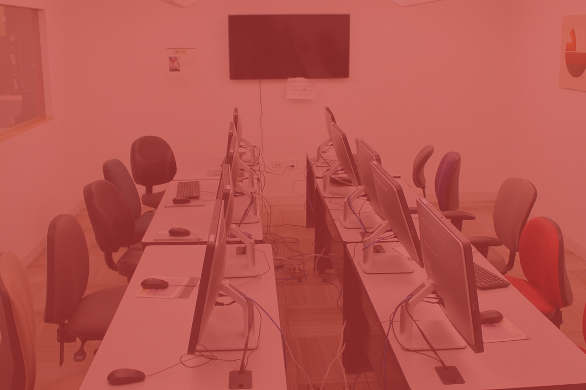 Computer lab with multiple computers and chairs, and a TV on the wall.
