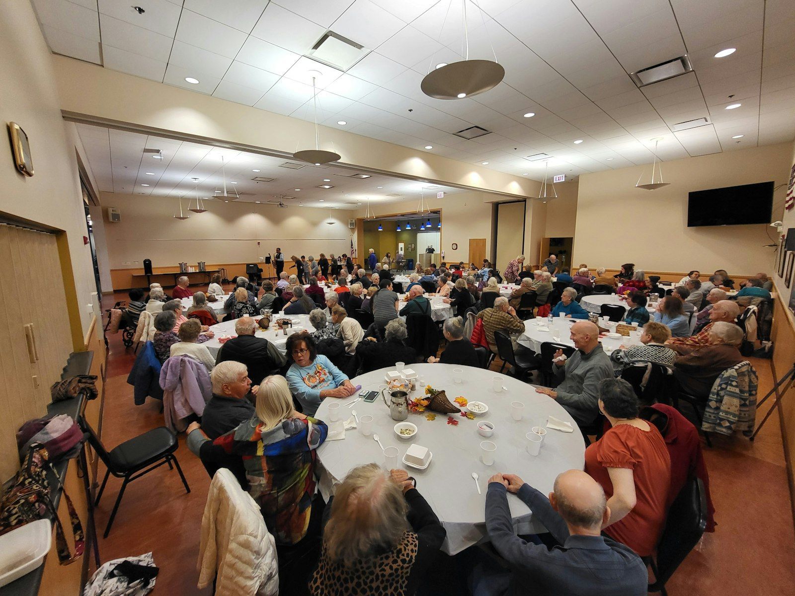 Large room with many people seated at round tables; a gathering or event in progress.