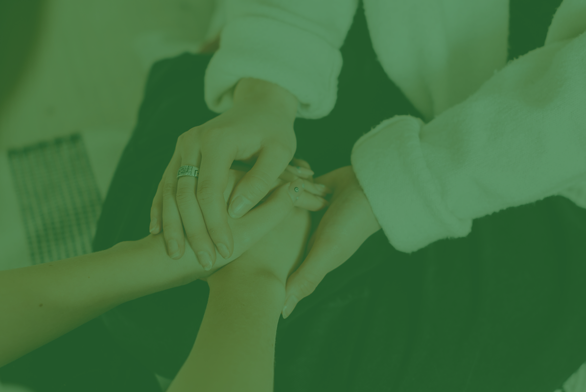 Hands holding each other, one hand has a ring. Person in white sleeves.