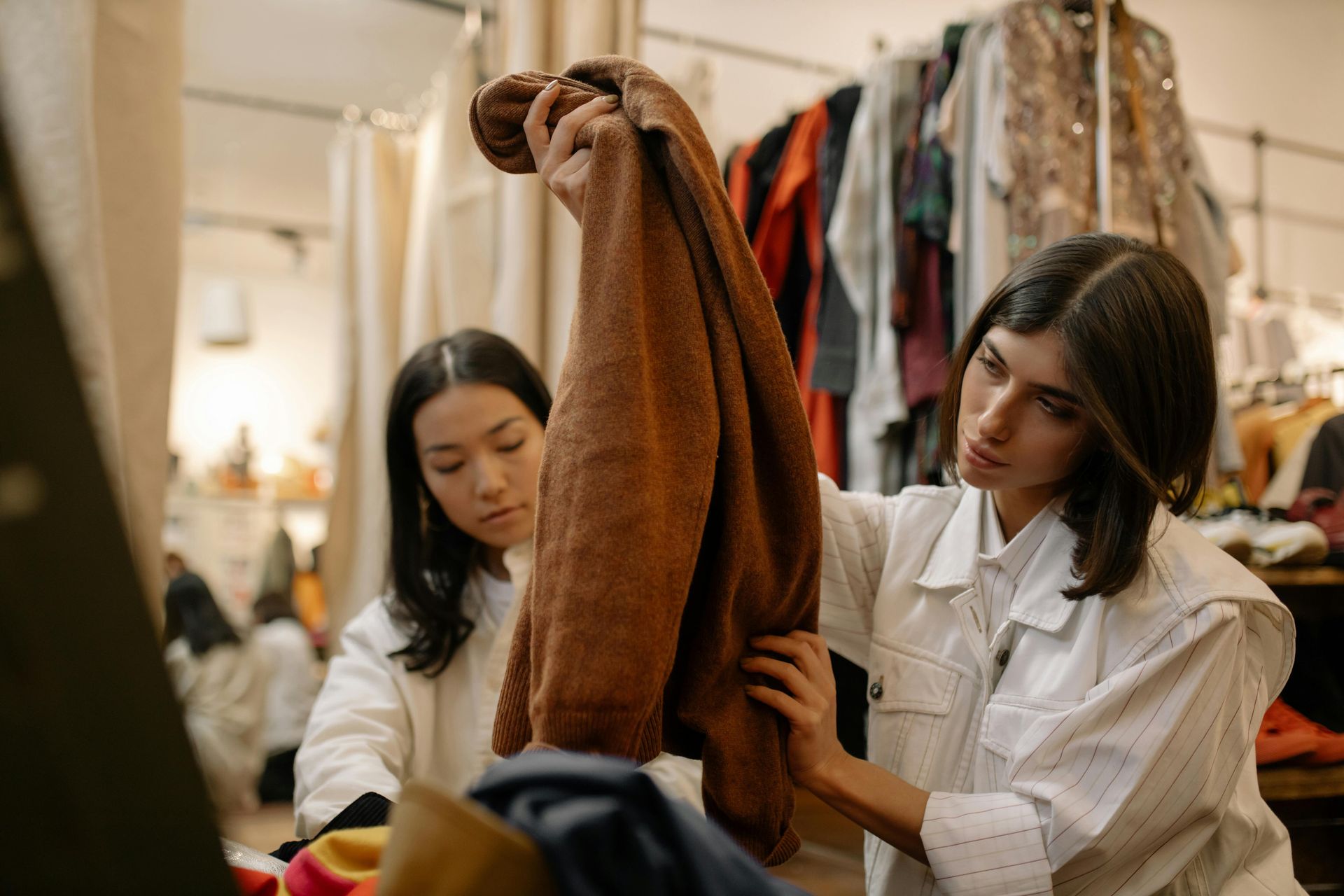 Two people examine a brown sweater in a clothing store.