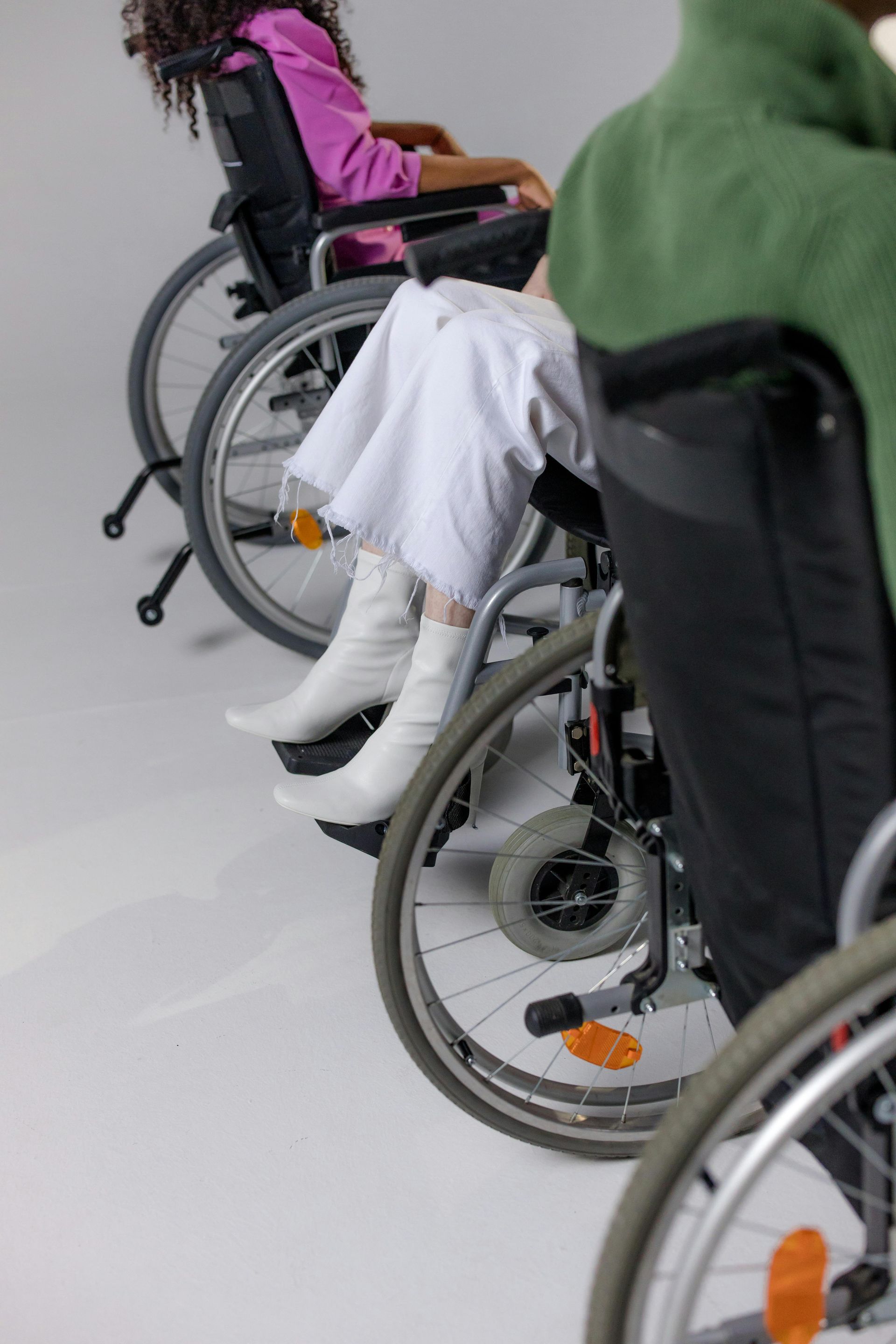 Three people in wheelchairs are lined up, each wearing different outfits, on a light gray background.