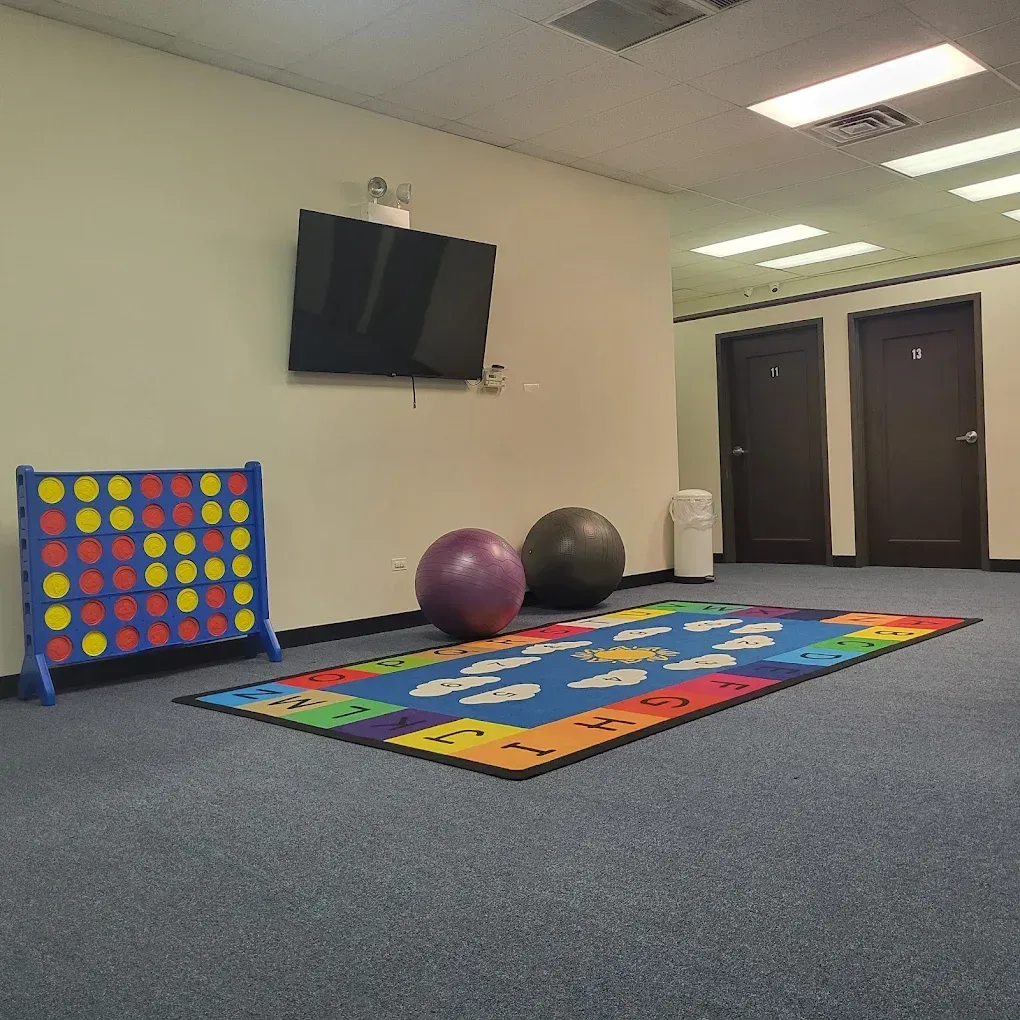 Quiet recreation room with wall TV, colorful mat, oversized game board, and large exercise balls on carpet.