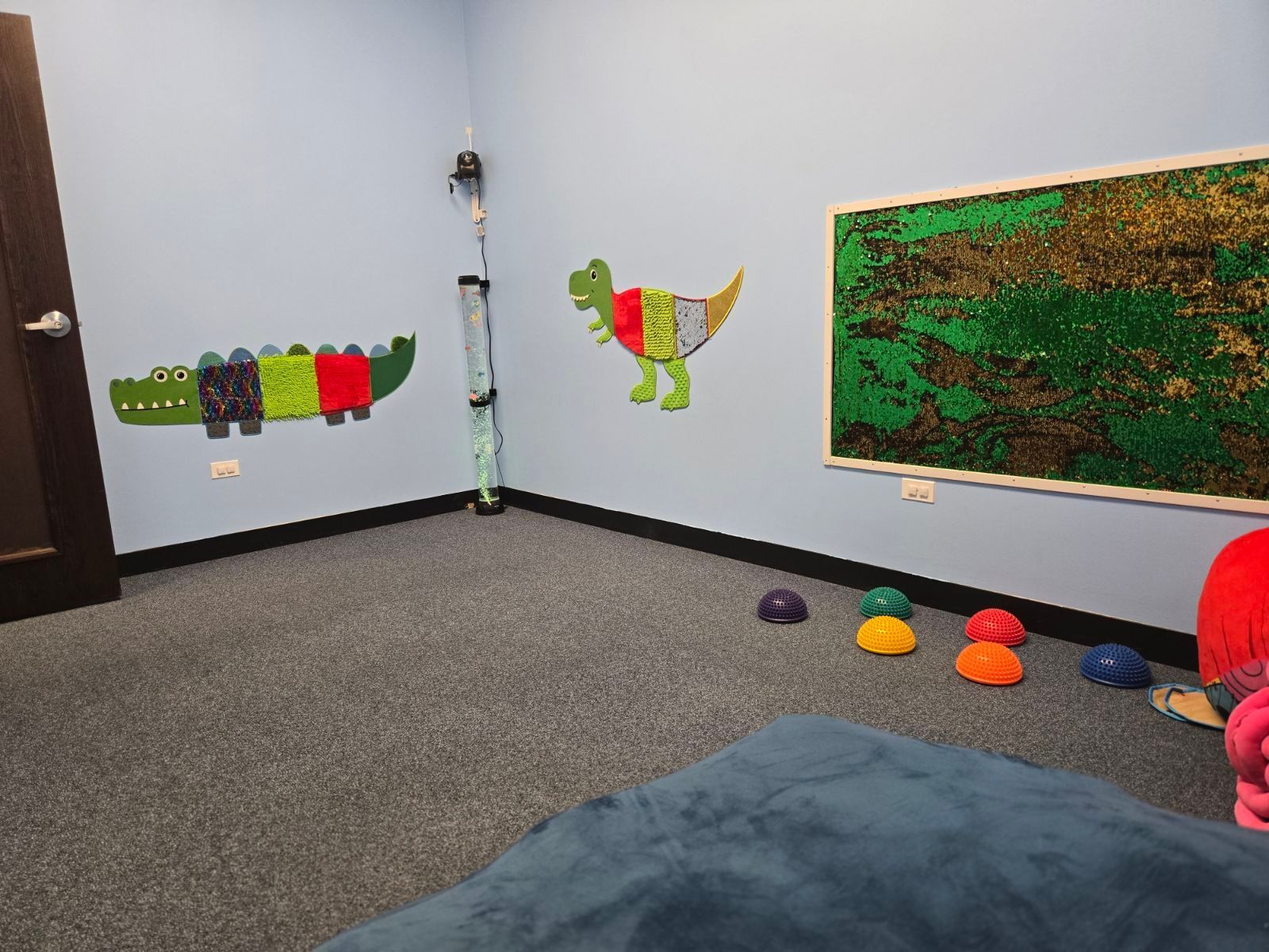Classroom corner with colorful wall art, beanbags, and scattered play balls on a gray carpet.