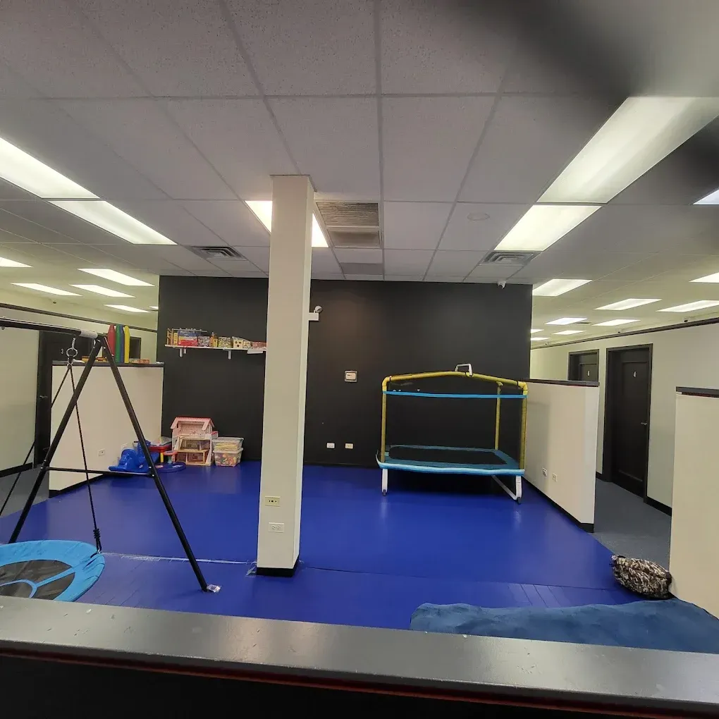 Empty office or gym room with blue floor mat, black walls, and trampoline equipment under fluorescent lights