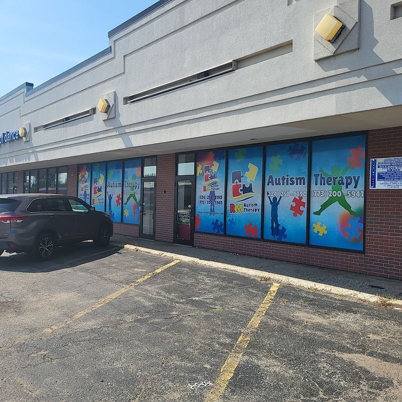 Storefront with colorful autism therapy window signs and a parked black SUV outside in a strip mall.