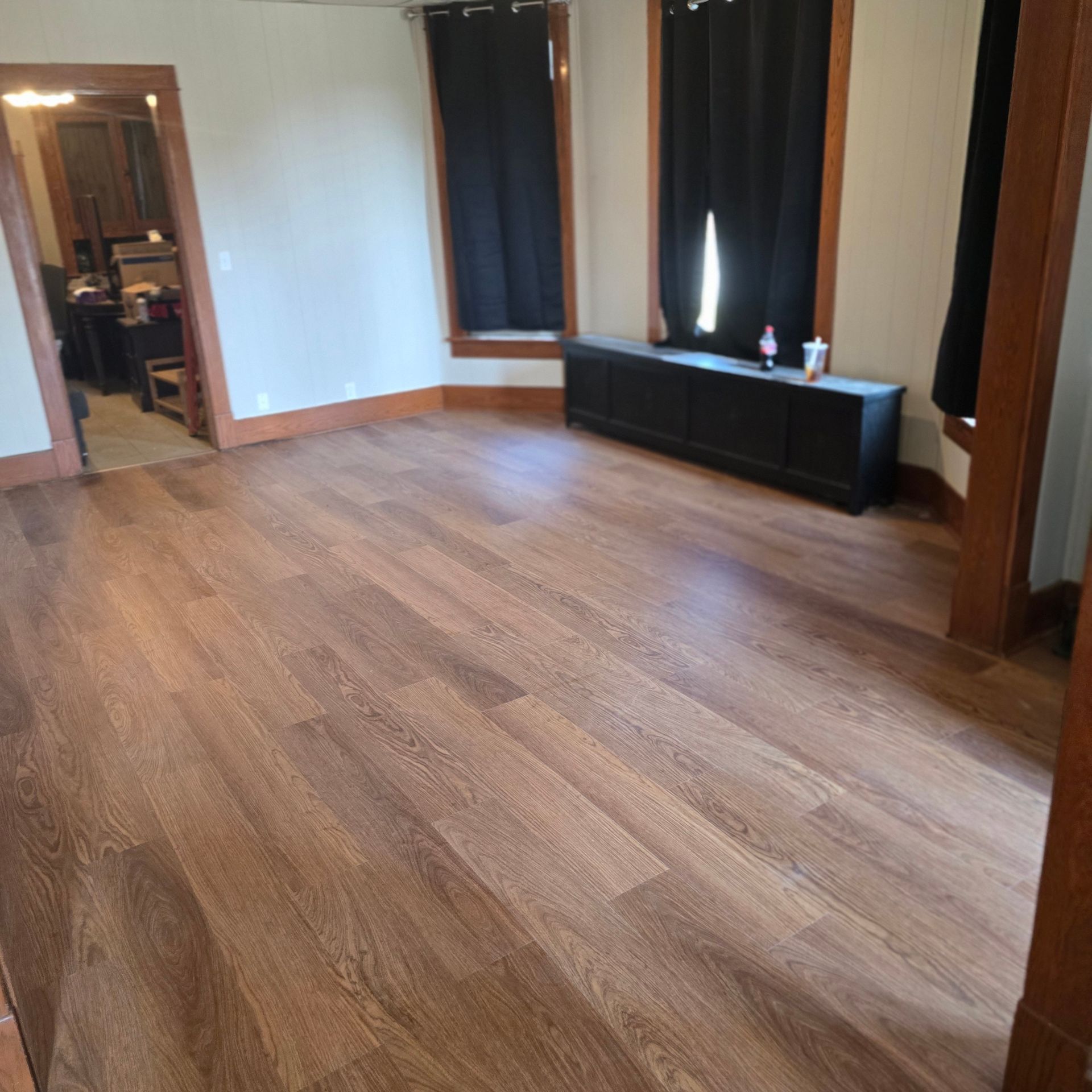 Empty room with dark wood-look flooring, black cabinet, and two windows with black curtains.