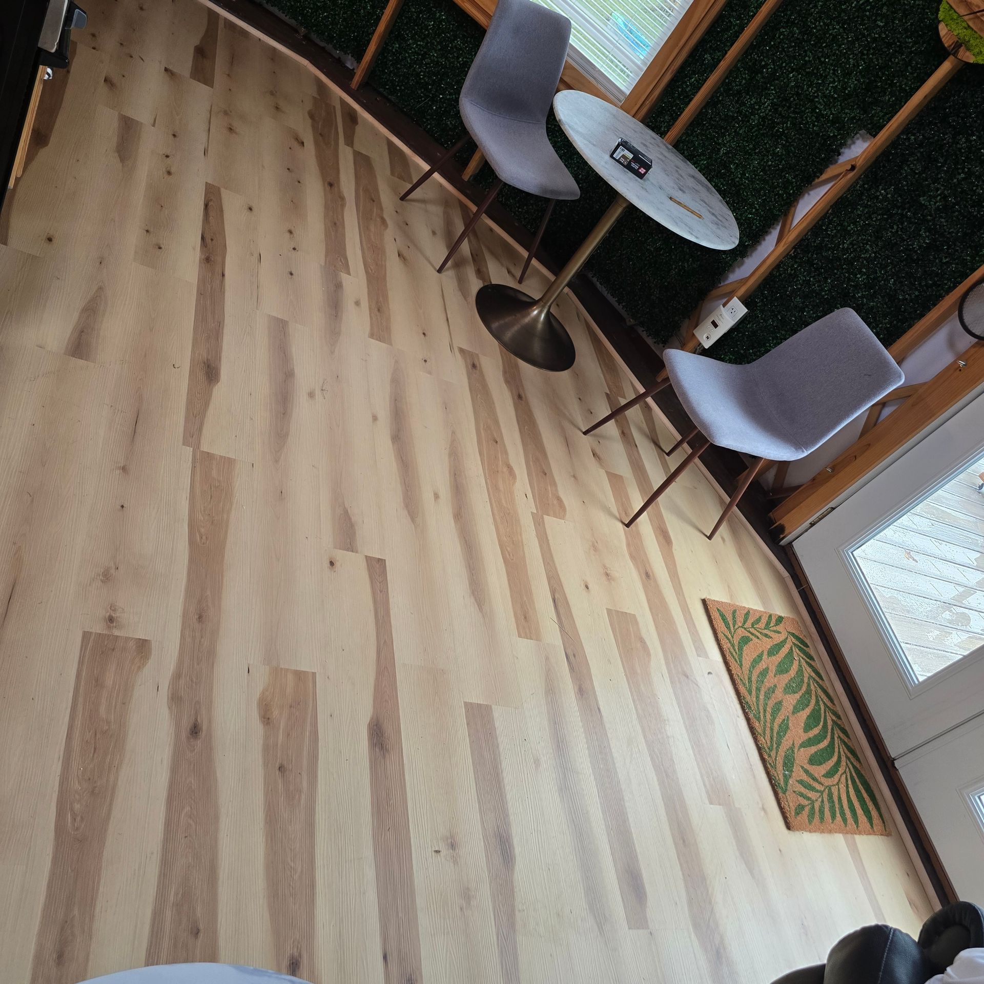 Wooden floor with two gray chairs, a small table, and a green rug in a room.