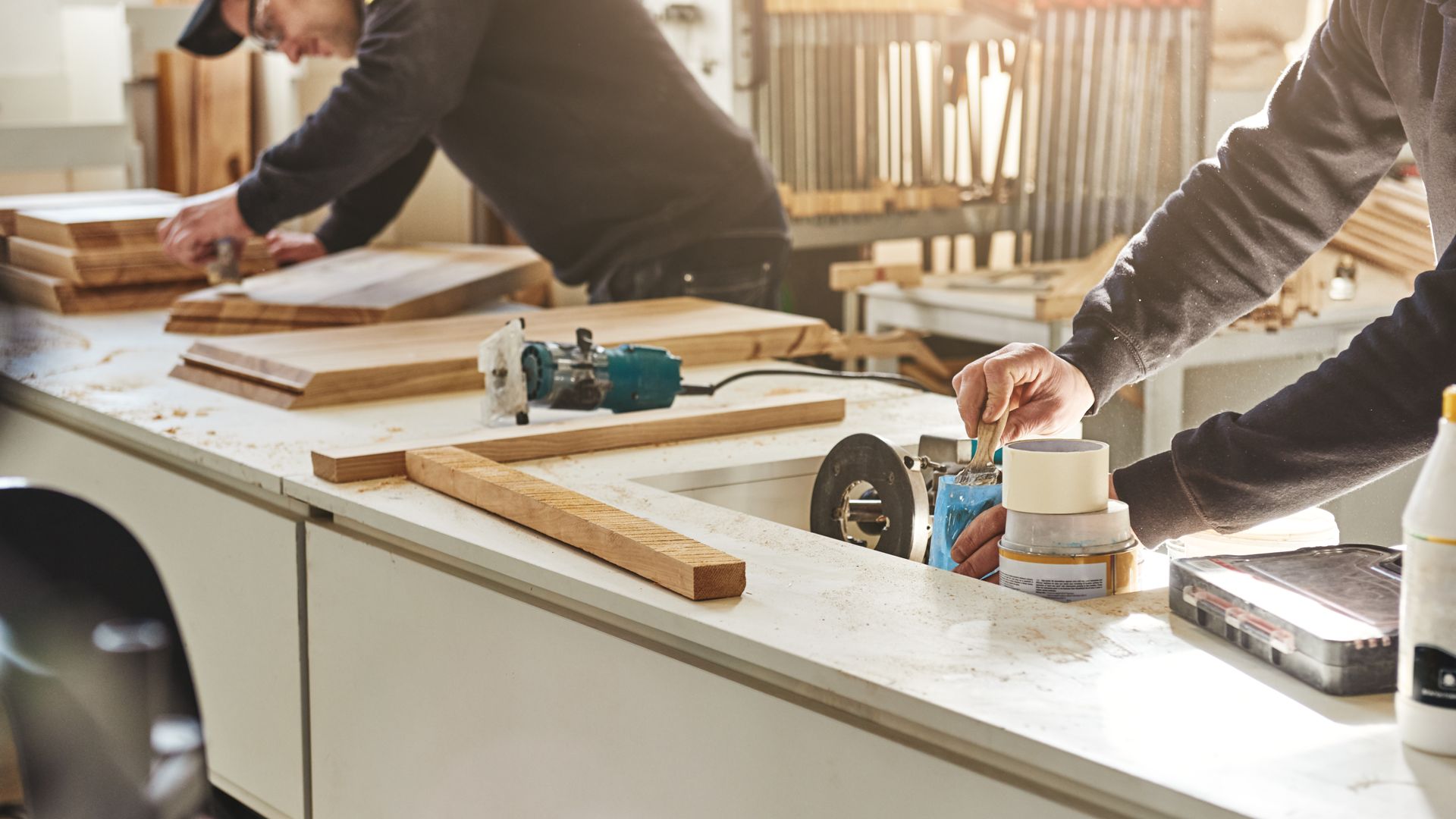 Two men are working on a piece of wood in a workshop.